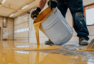 a professional technician from Concrete Etc carefully pouring an epoxy coating onto a concrete floor